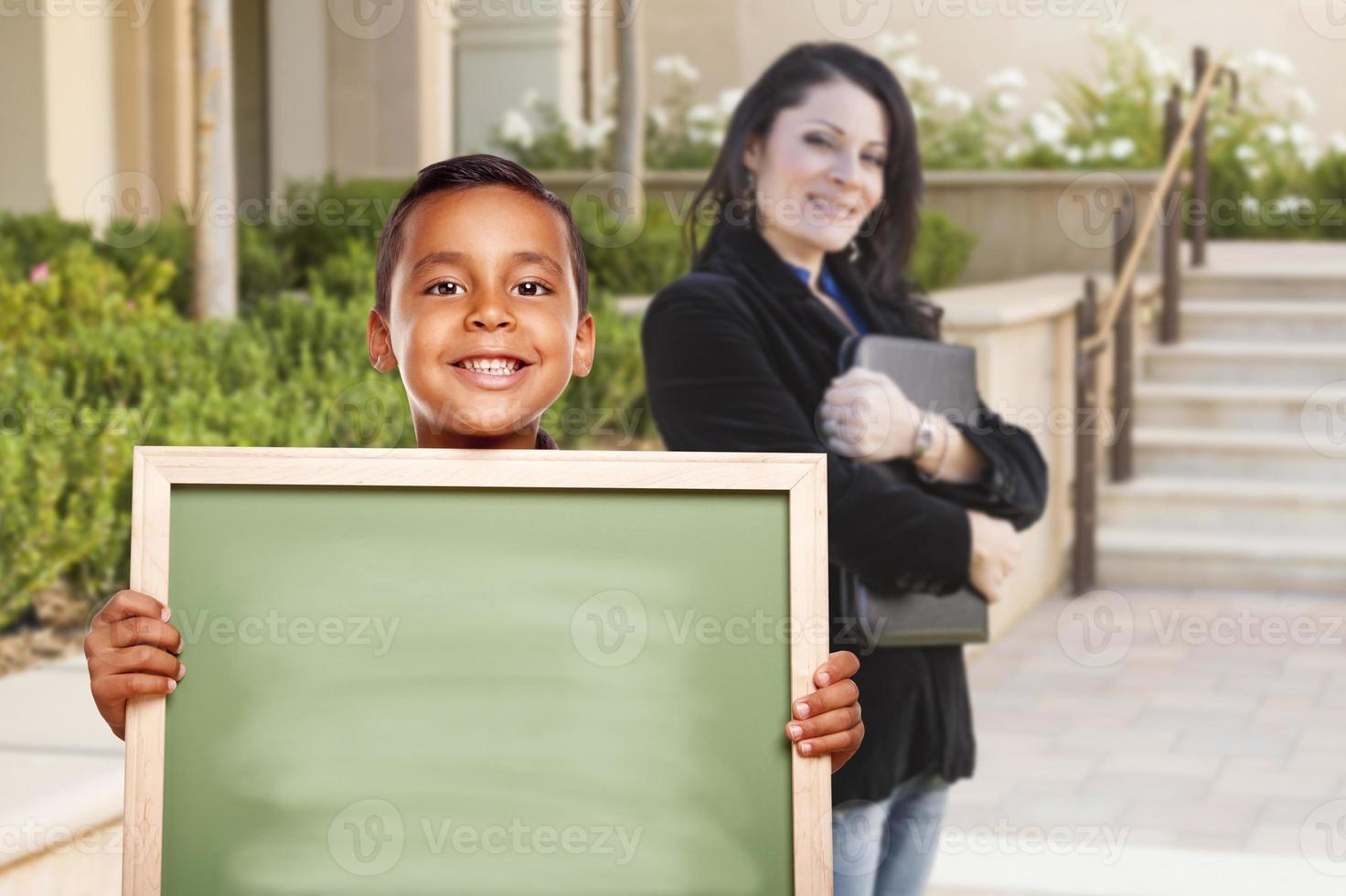 menino segurando quadro de giz em branco no campus com professor atrás foto