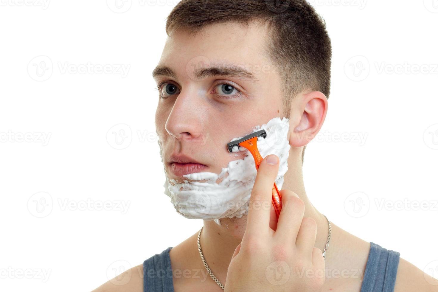 retrato de um jovem bonito com espuma no rosto que raspa cuidadosamente sua máquina de barba close-up foto