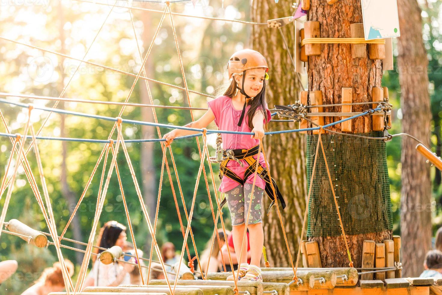 adorável menina aproveitando seu tempo na escalada do parque de aventura em um dia quente e ensolarado de verão. atividades de verão para crianças pequenas. criança se divertindo nas férias escolares. foto