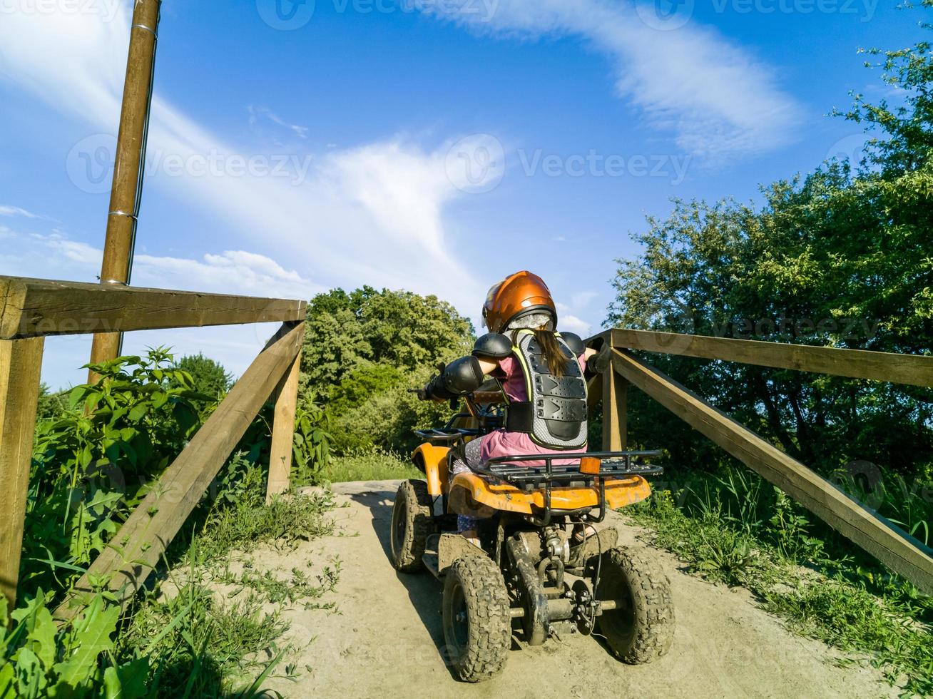 a menina anda de quadriciclo. uma mini moto-quatro é uma garota legal em um capacete e roupas de proteção. carro elétrico de quadriciclo elétrico para crianças populariza tecnologia verde foto