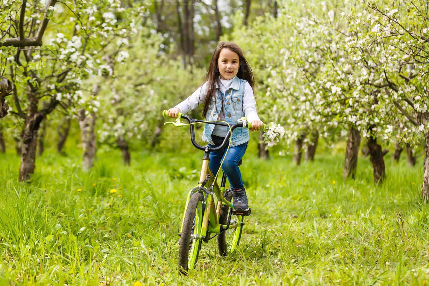 menina com bicicleta perto de árvores floridas na primavera foto