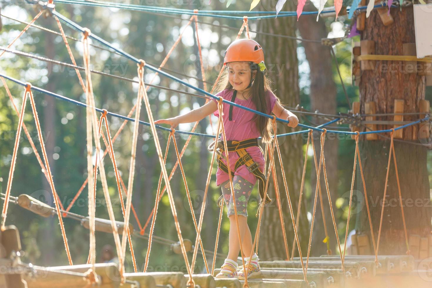 adorável menina aproveitando seu tempo na escalada do parque de aventura em um dia quente e ensolarado de verão. atividades de verão para crianças pequenas. criança se divertindo nas férias escolares. foto