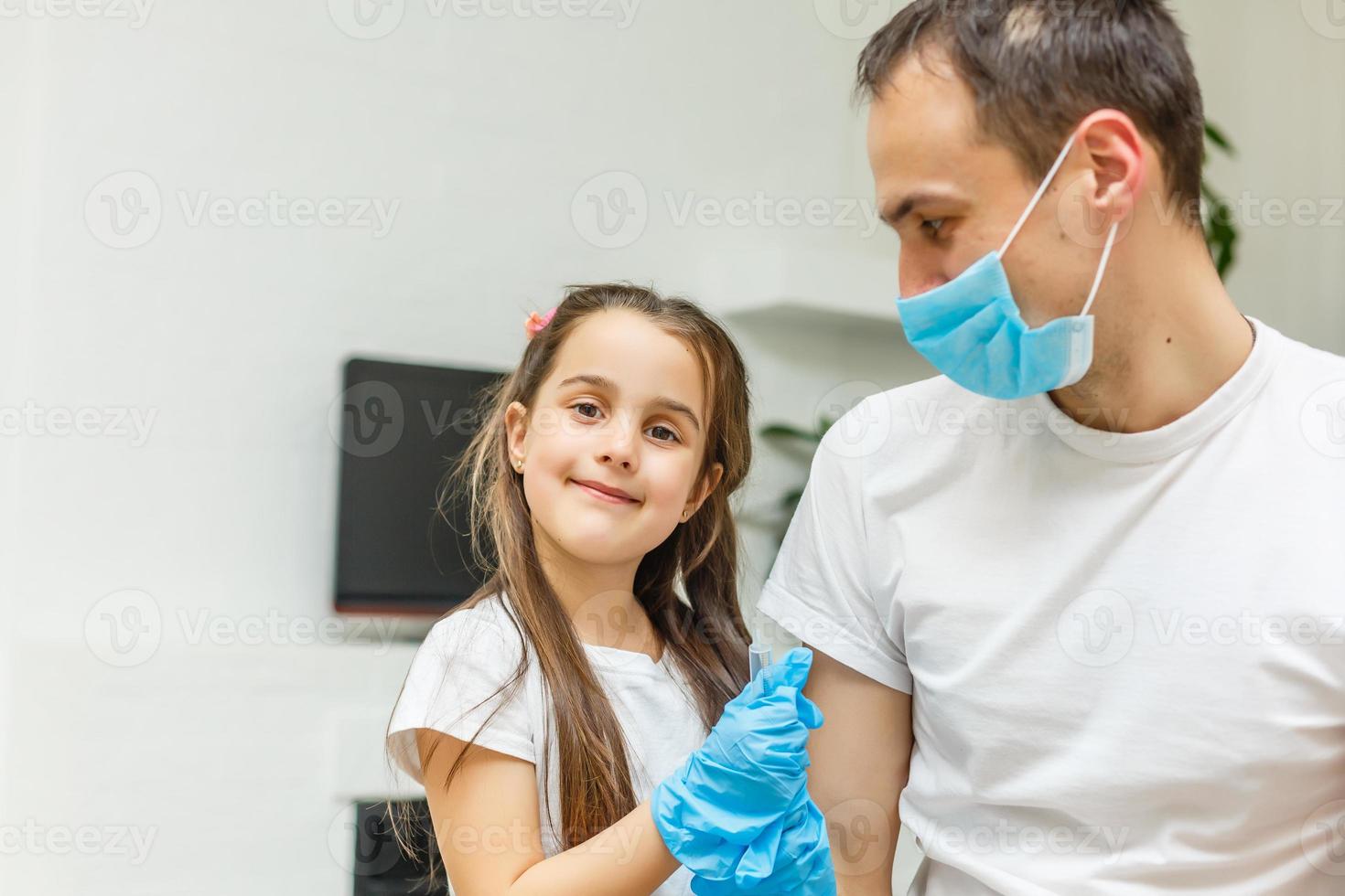 filhinha brincalhona jogando um jogo engraçado como médico se divertindo com o pai sentado no sofá, menina bonita fingindo enfermeira em uniforme médico segurando estetoscópio ouvindo pai paciente em casa foto