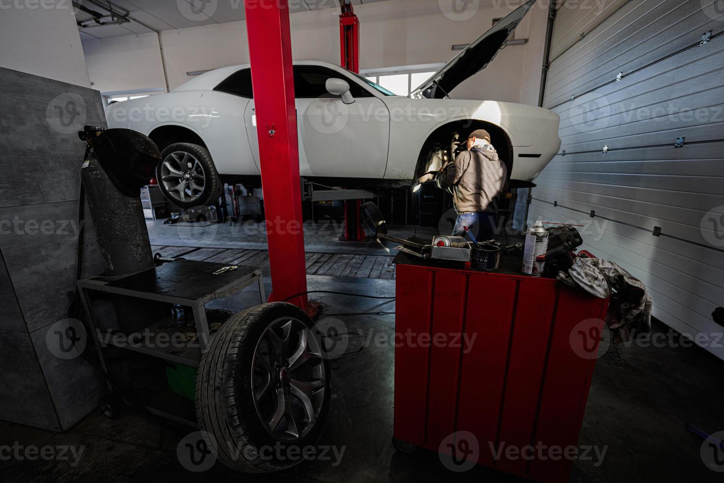 mecânico na estação de reparo de serviço trabalhando com muscle car, desmonta uma roda no elevador. foto