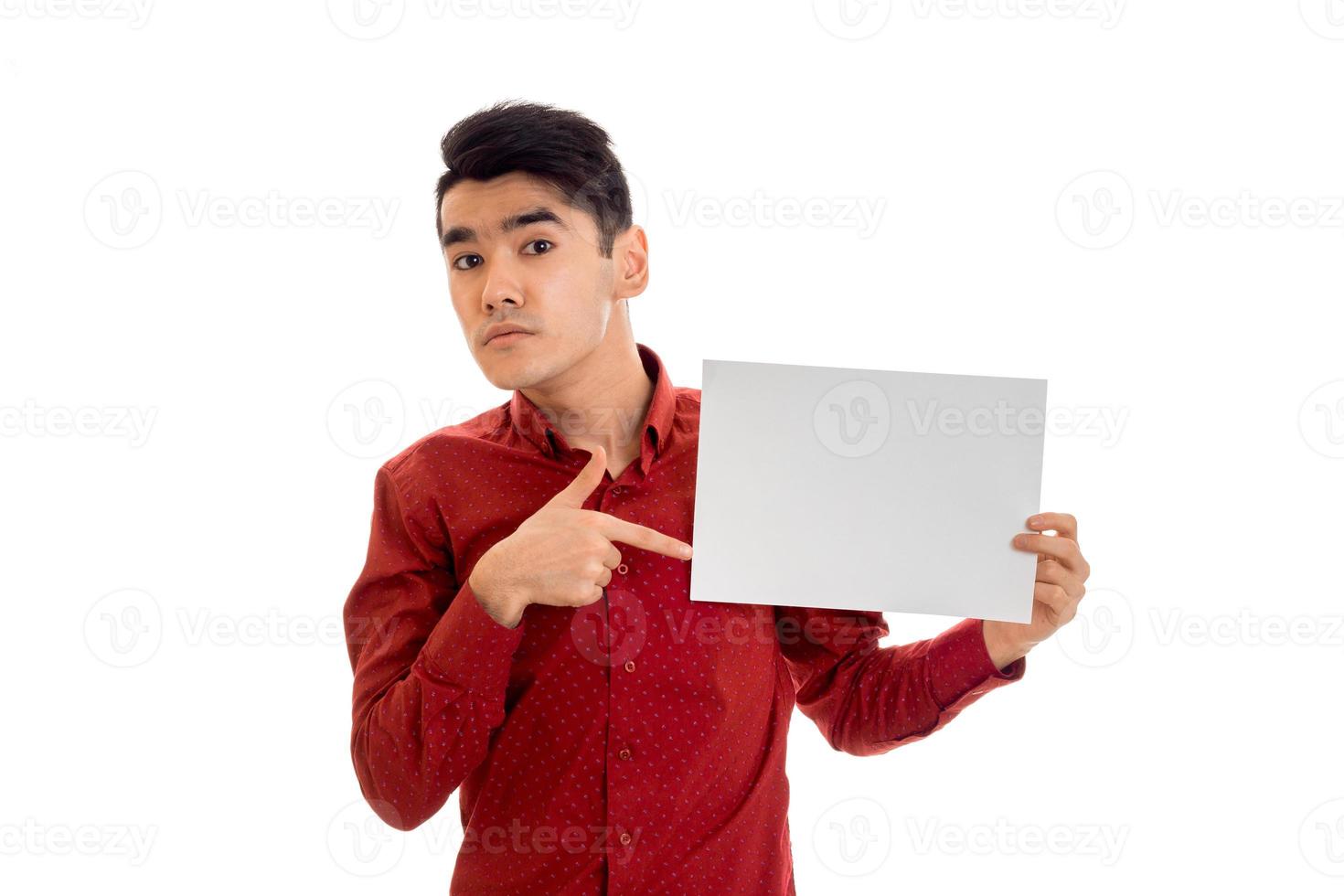 youn engraçado morena modelo masculino na camisa vermelha posando com um cartaz vazio nas mãos e olhando para a câmera isolada no fundo branco foto