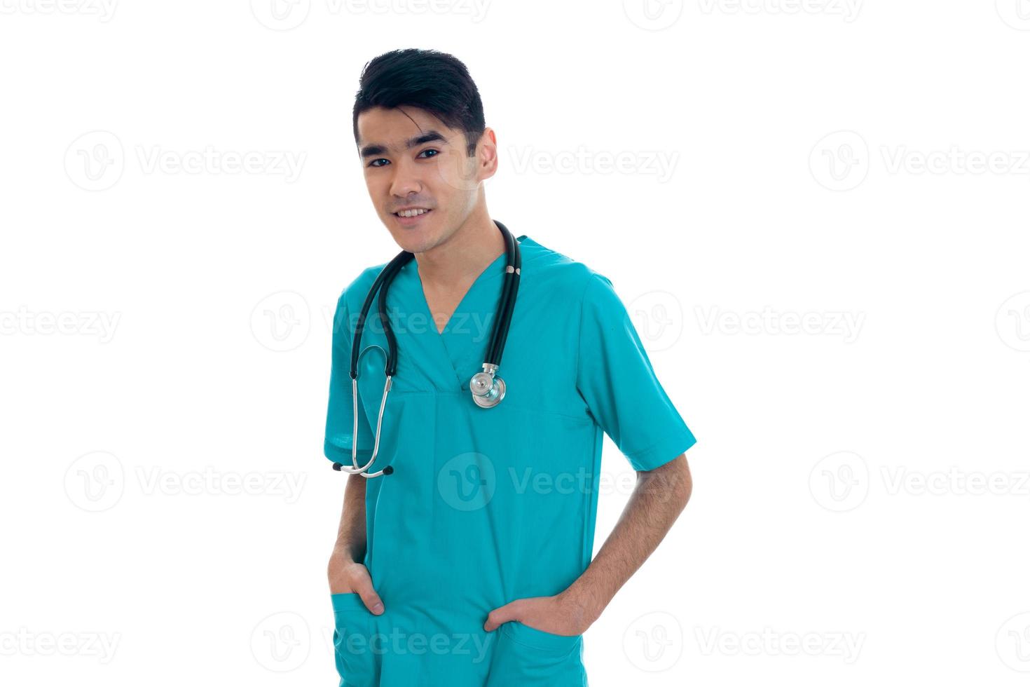 médico bonito e elegante em uniforme azul com estetoscópio posando e sorrindo para a câmera isolada no fundo branco foto