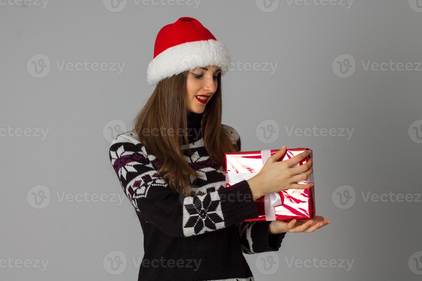 mulher de suéter quente e chapéu de Papai Noel com presente vermelho foto