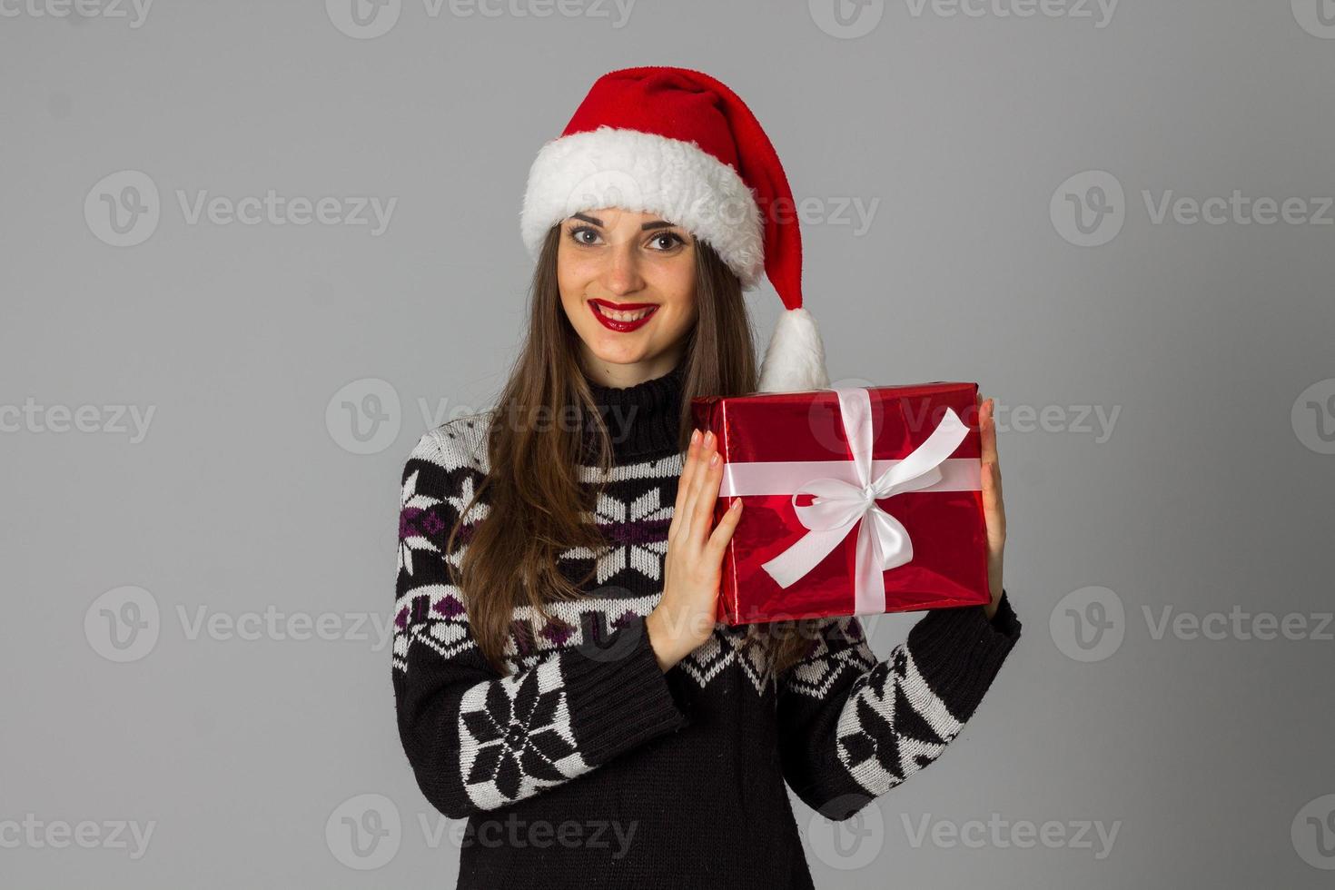 mulher de suéter quente e chapéu de Papai Noel com presente vermelho foto