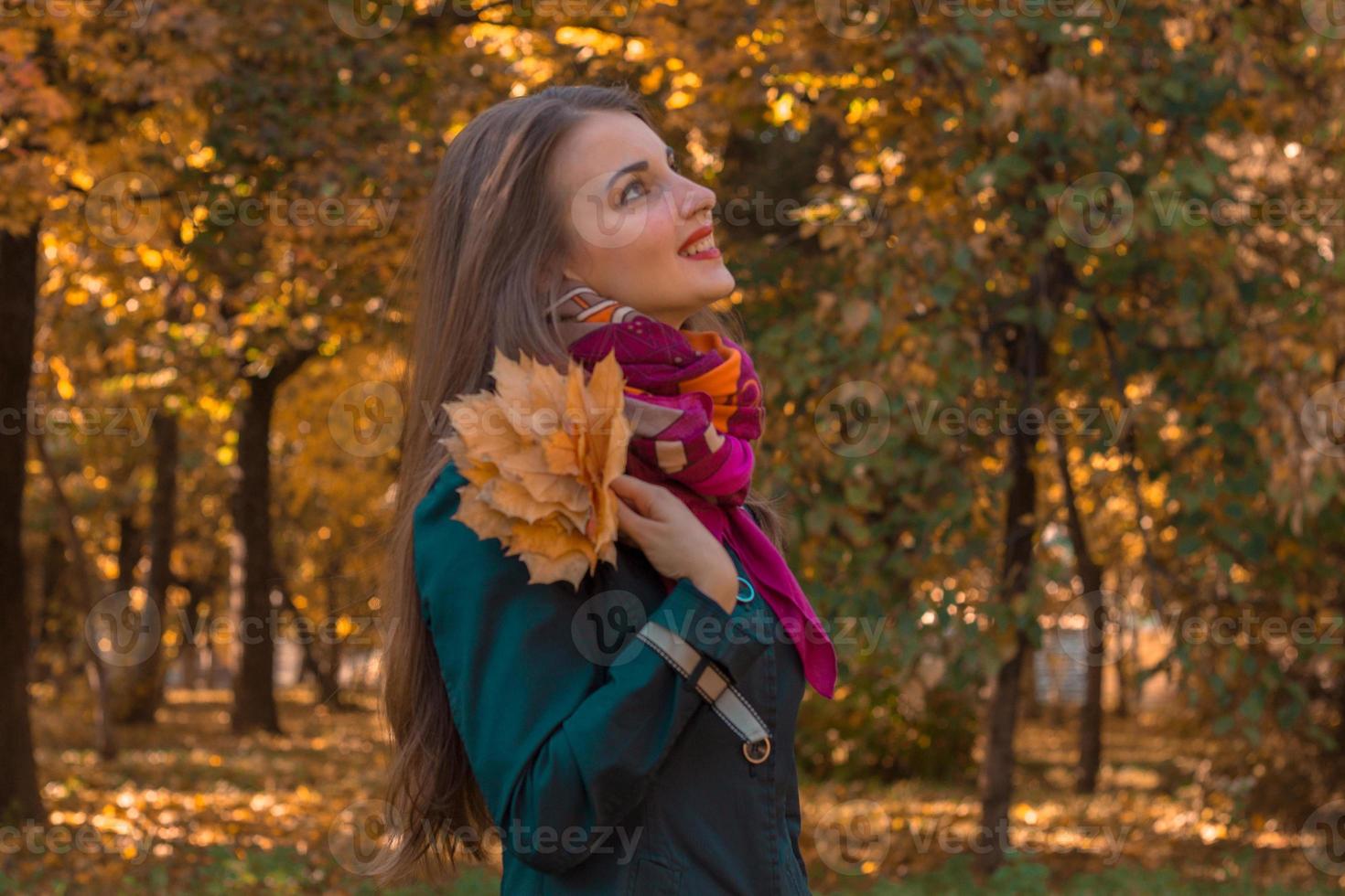 linda garota com cachecol rosa fica de lado no parque e mantém as folhas na mão foto