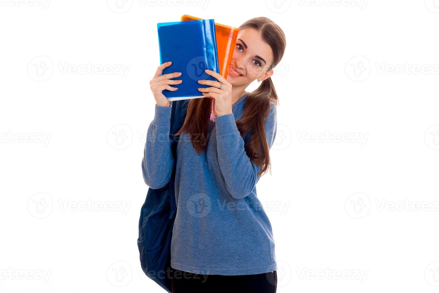 linda garota de jovens estudantes com mochila e pastas para cadernos nas mãos dela olhando para a câmera e sorrindo isolado no fundo branco foto