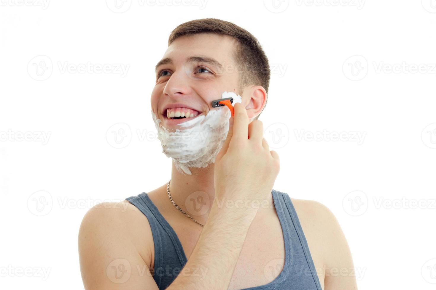 um jovem alegre com espuma no rosto olha para a máquina e faz a barba foto