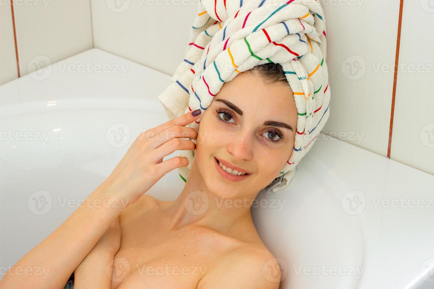 uma jovem maravilhosa com toalha no cabelo está na banheira e um sorriso foto