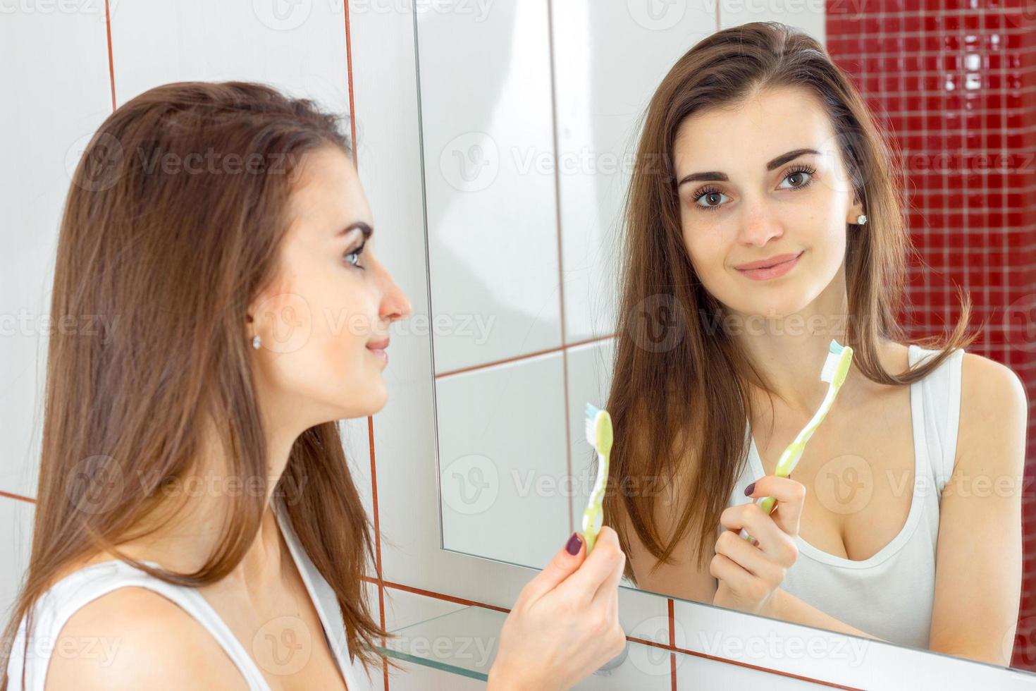 jovem mulher bonita escovando os dentes na frente do espelho foto