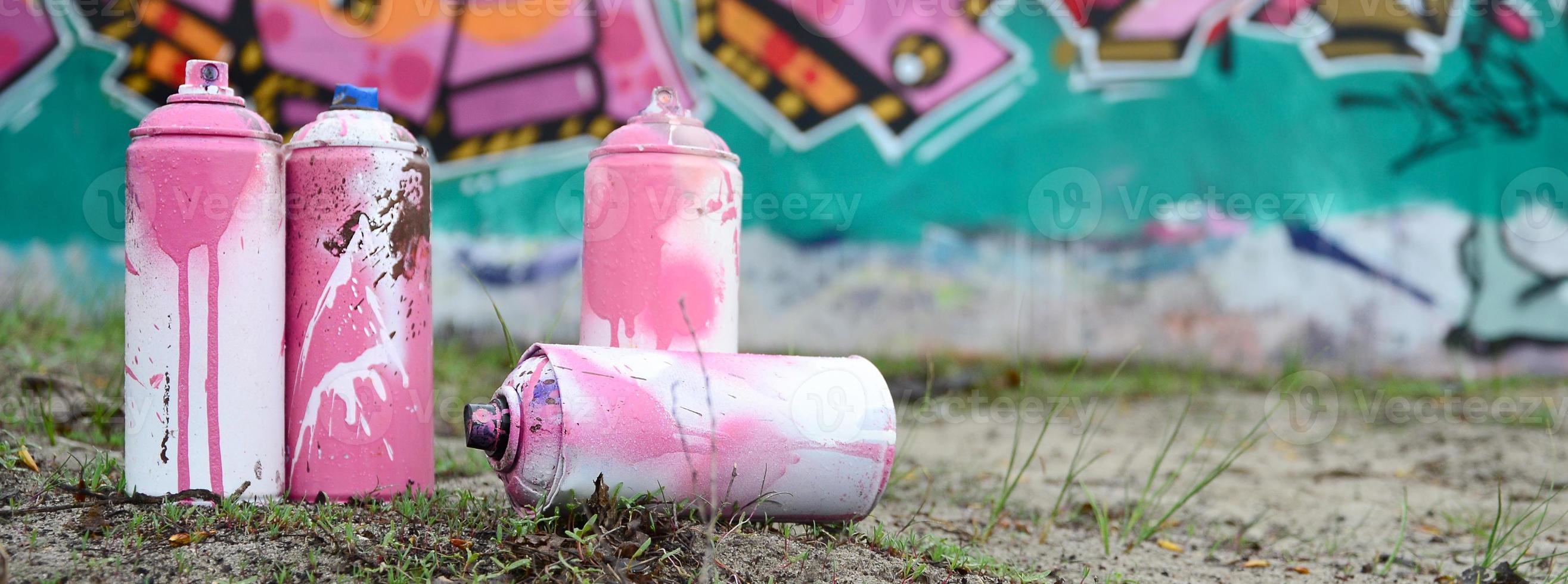 algumas latas de tinta usadas estão no chão perto da parede com uma bela pintura de grafite nas cores rosa e verde. conceito de arte de rua foto