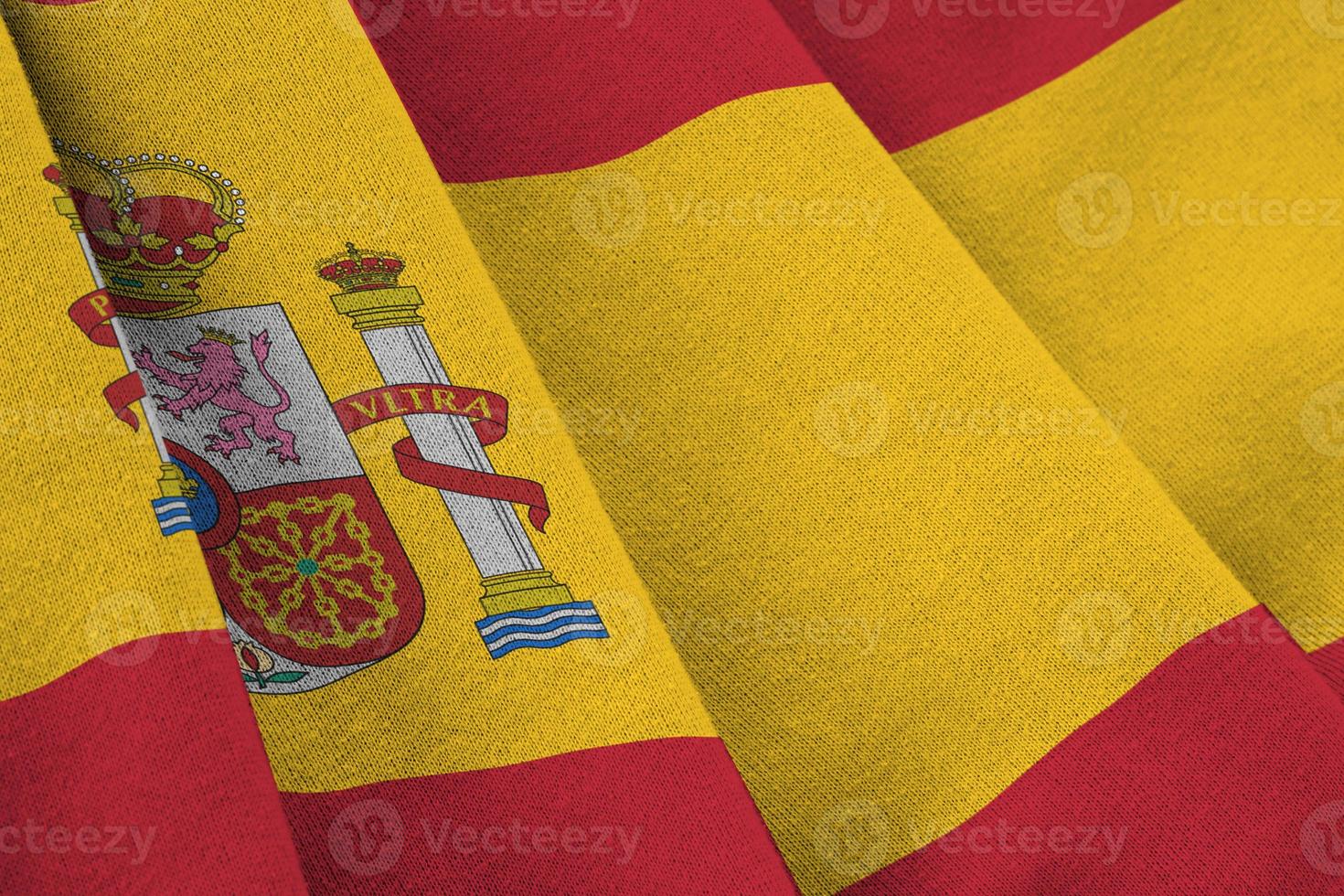 bandeira da espanha com grandes dobras acenando perto sob a luz do estúdio dentro de casa. os símbolos e cores oficiais no banner foto