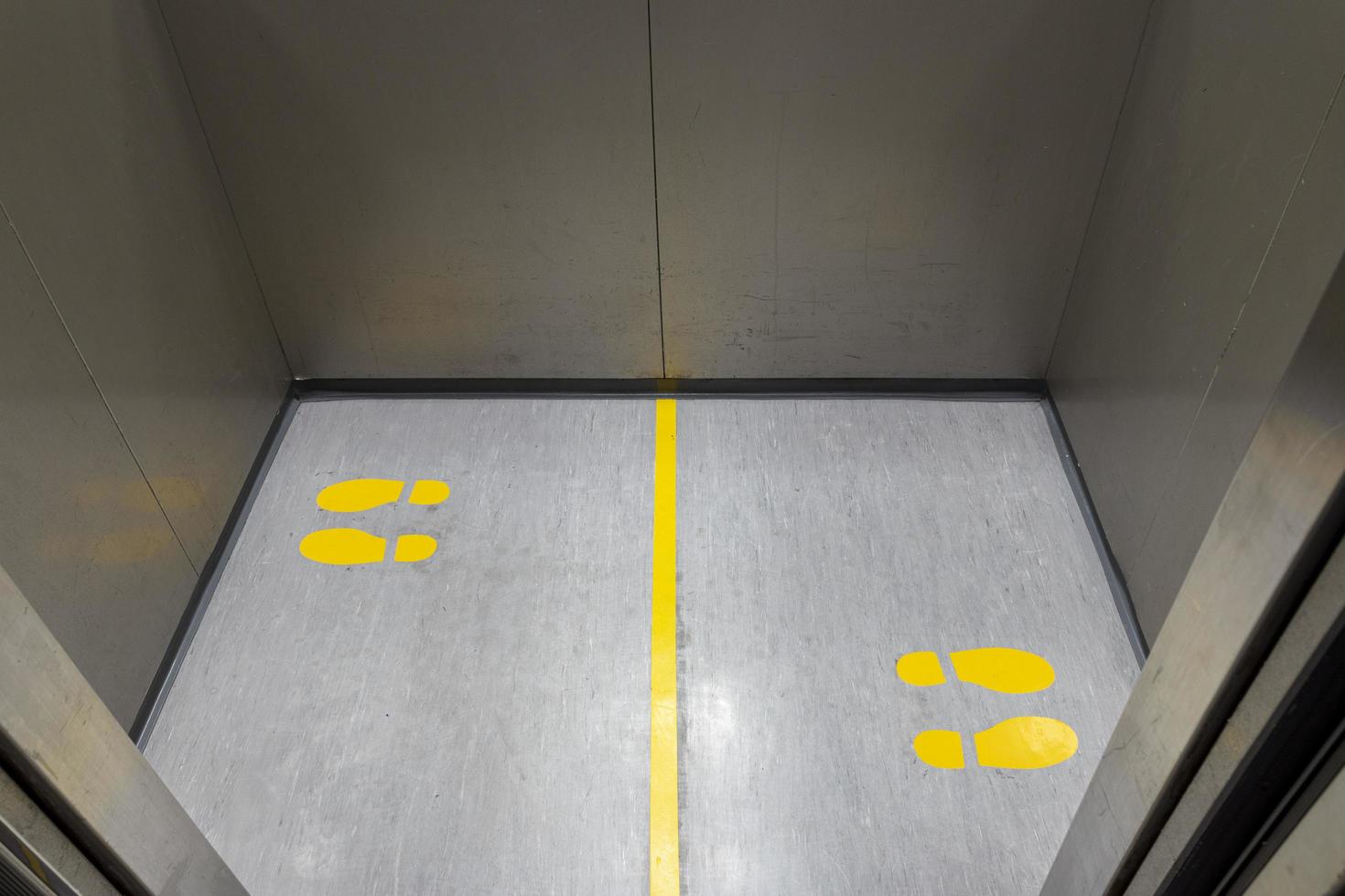 distanciamento social para covid-19 com placa de pegada amarela em elevador público foto