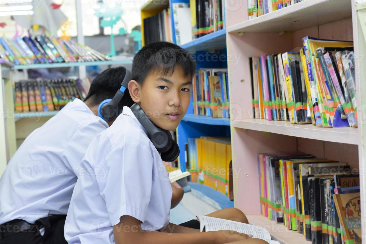 fucus suave de dois estudantes asiáticos estão ouvindo mídia, lendo e consultando sobre o livro favorito na biblioteca da escola foto