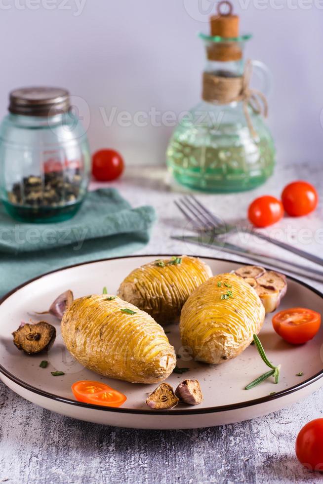 deliciosas batatas hasselback assadas caseiras com alho e alecrim em um prato. visão vertical foto