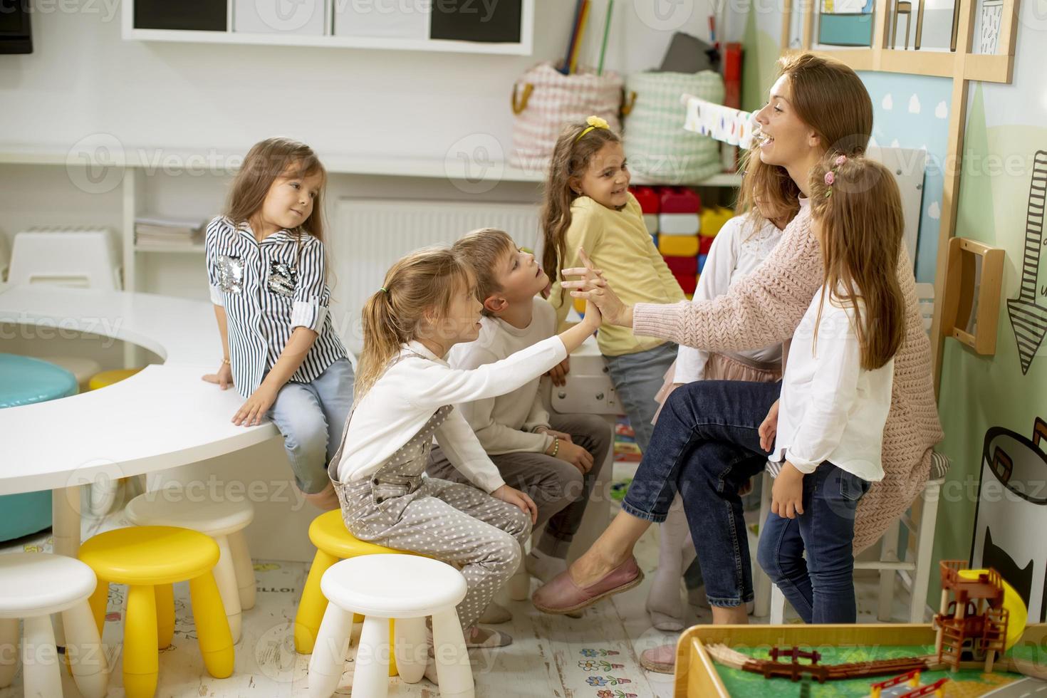 crianças fofas da pré-escola juntam as mãos com a professora do berçário foto