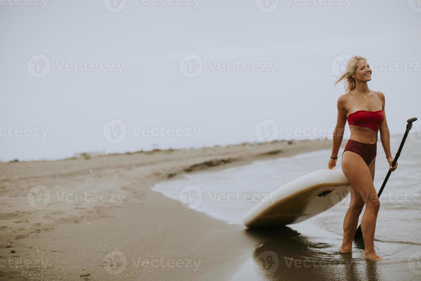jovem mulher com prancha de remo na praia em um dia de verão foto