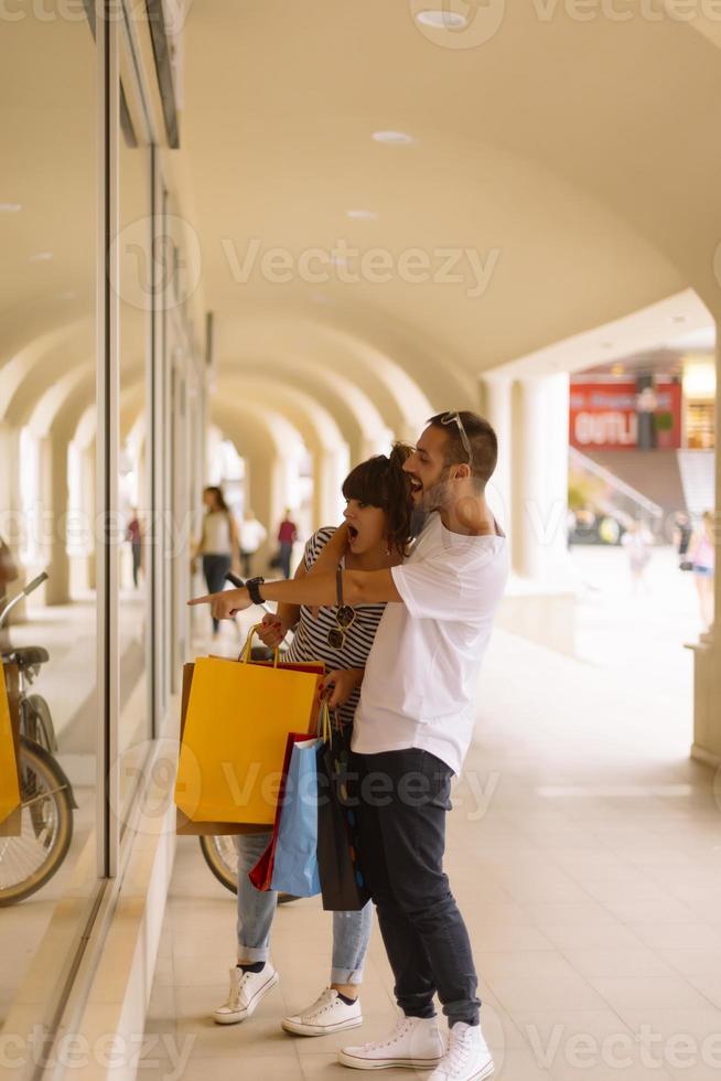 retrato de um jovem casal caucasiano alegre homem e mulher segurando muitos sacos de papel depois de fazer compras enquanto caminhava e conversava na rua. casal de família feliz com pacotes ao ar livre. conceito de compra foto