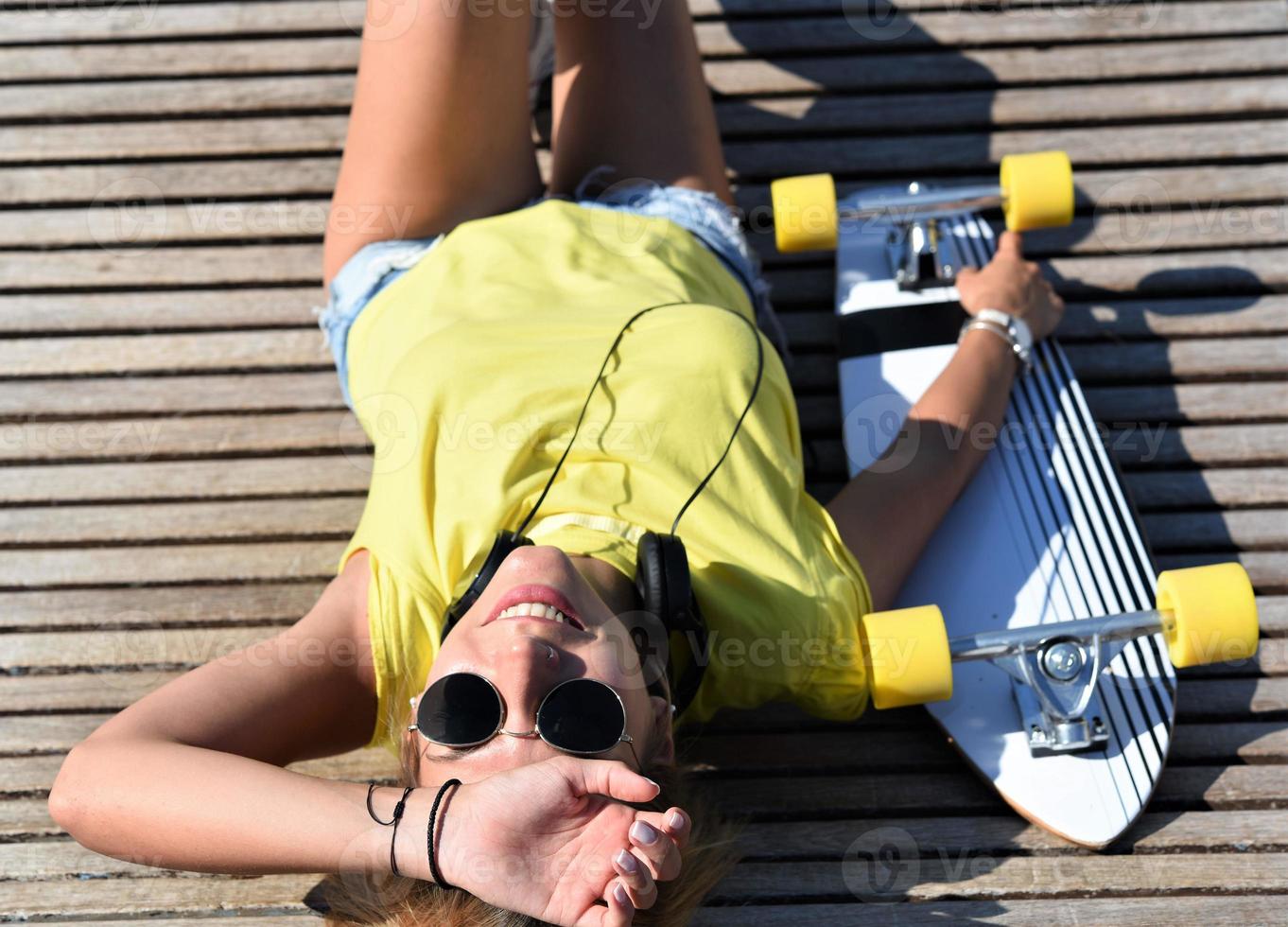 elegante jovem urbana com longboard deitado no banco de madeira foto