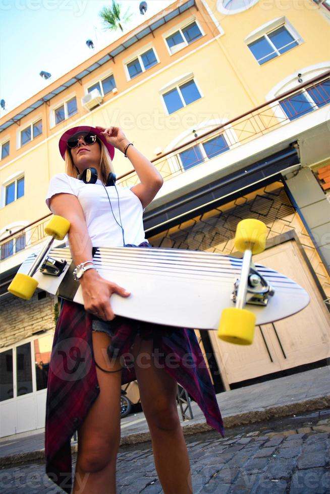 menina linda hipster com skate usando óculos escuros na cidade. foto