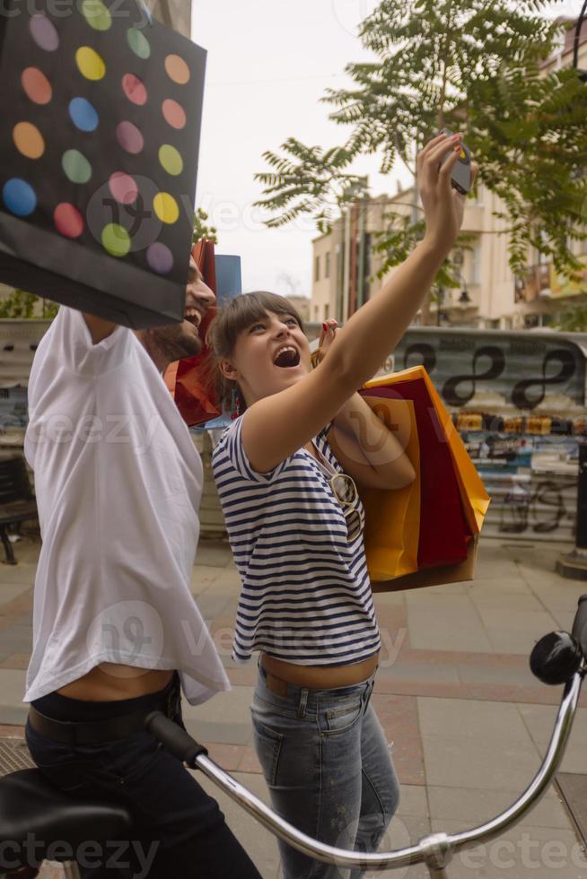 retrato de um jovem casal caucasiano alegre homem e mulher segurando muitos sacos de papel depois de fazer compras enquanto caminhava e conversava na rua. casal de família feliz com pacotes ao ar livre. conceito de compra foto