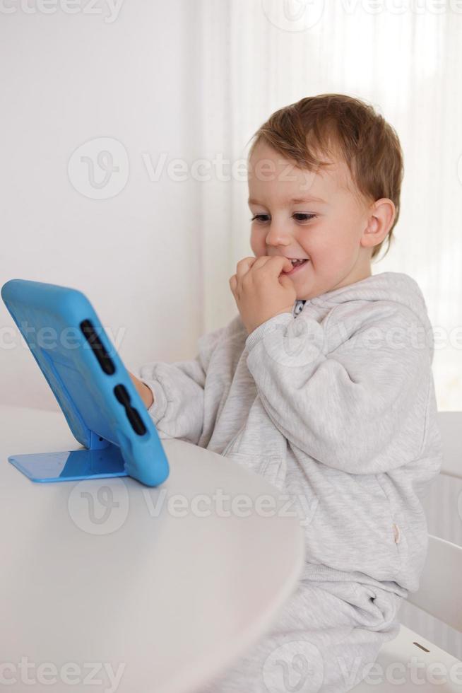 menino feliz jogando jogo no tablet digital em casa. retrato de uma criança em casa assistindo desenho animado no tablet. criança moderna e tecnologia educacional. foto