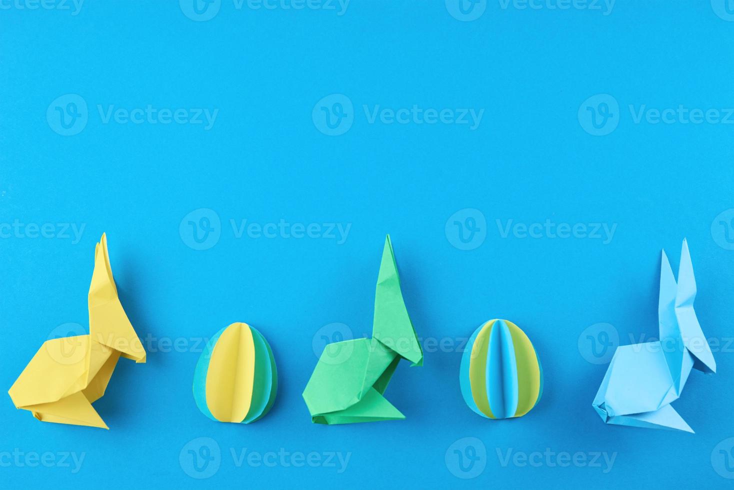 coelhos esater de papel origami e ovos coloridos em fundo azul foto