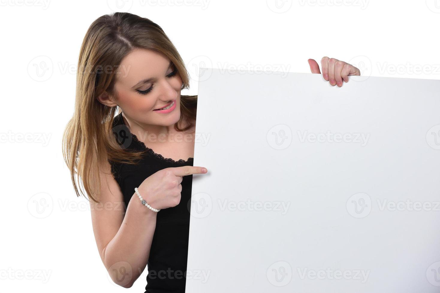 retrato de uma jovem mulher bonita espiando a câmera segurando placa branca em branco foto