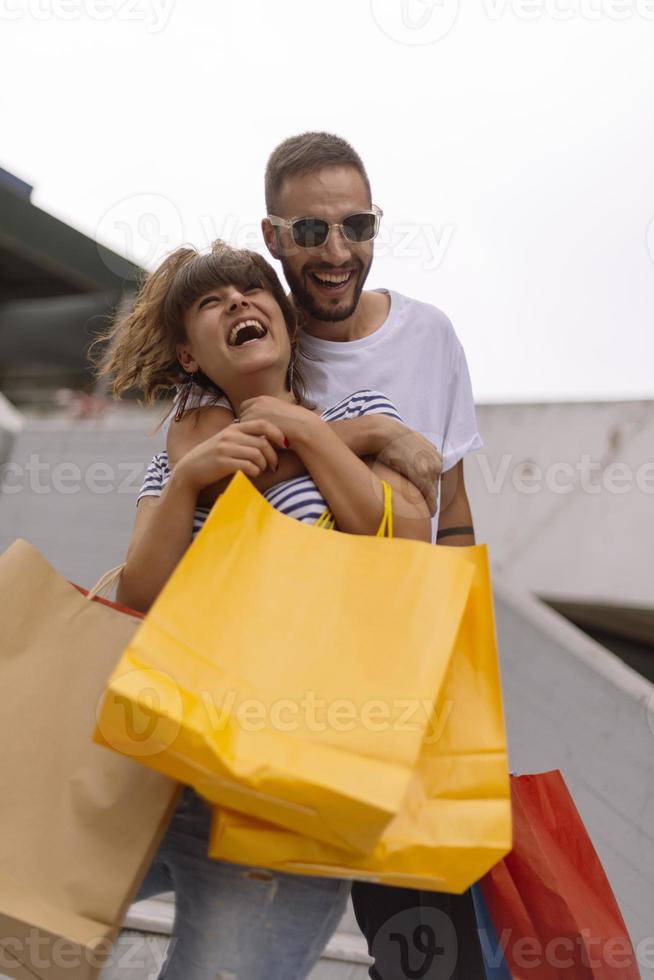 retrato de um jovem casal caucasiano alegre homem e mulher segurando muitos sacos de papel depois de fazer compras enquanto caminhava e conversava na rua. casal de família feliz com pacotes ao ar livre. conceito de compra foto