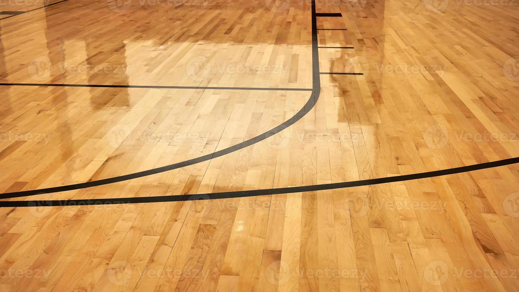 interior da quadra esportiva vazia de basquete moderno, piso de madeira com revestimento semibrilhante, luzes artificiais refletidas foto