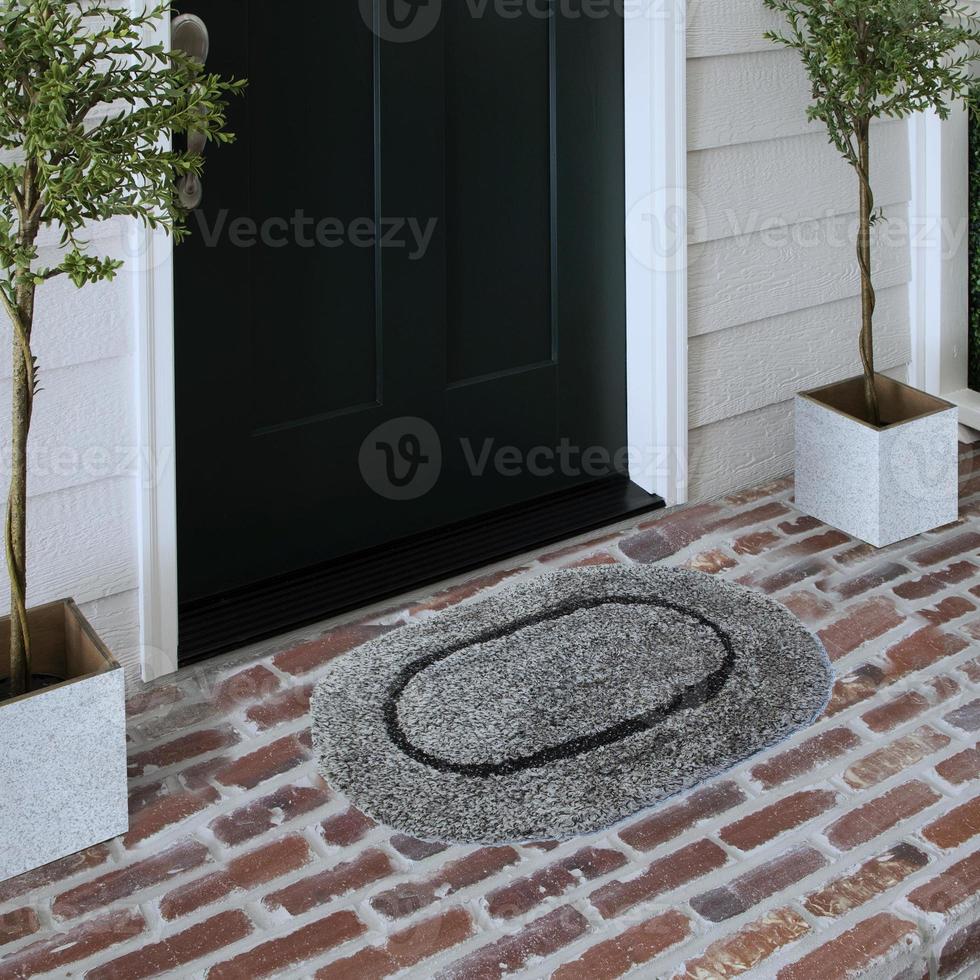 capacho de entrada de boas-vindas de design colocado no piso de tijolo sólido do lado de fora da porta de entrada com plantas foto