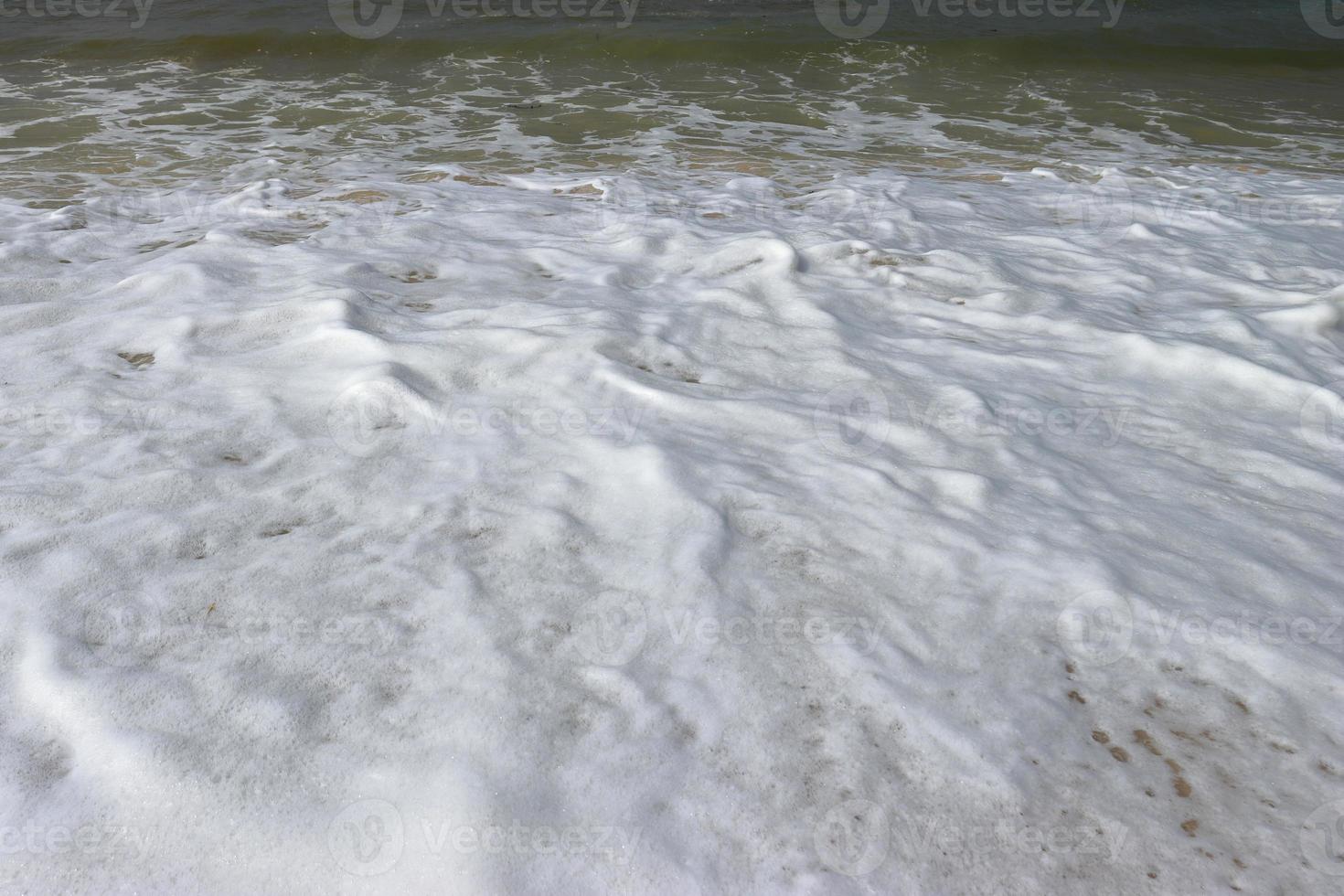 espuma de água com areia lisa. ondas na costa da bela praia de areia tropical em um dia ensolarado foto