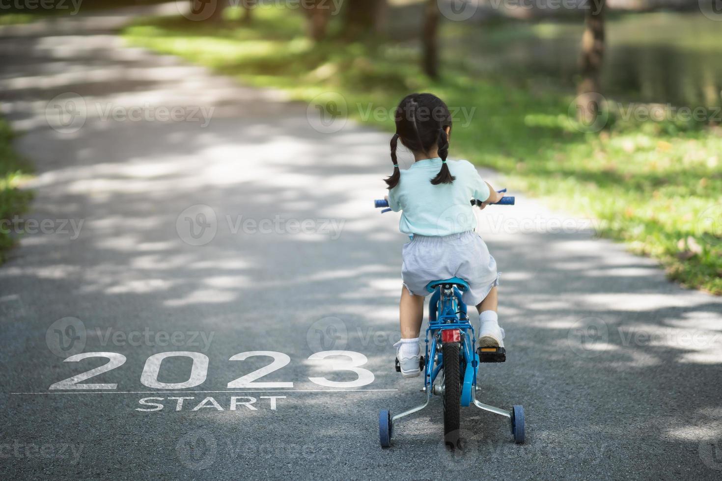 feliz ano novo 2023,2023 simboliza o início do ano novo. a carta começa o ano novo de 2023 na bicicleta de bicicleta da menina na estrada no jardim do parque natural. meta de sucesso. papel de parede do número 2023. foto
