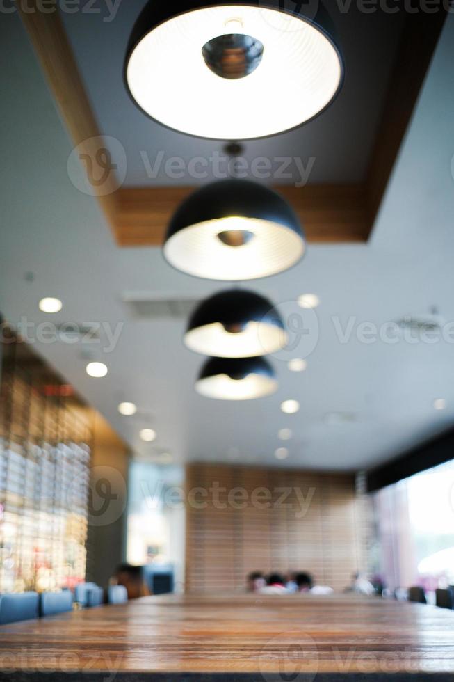 feche a borda da mesa de madeira no café com fundo desfocado da moderna sala de design de interiores e lâmpada de iluminação foto