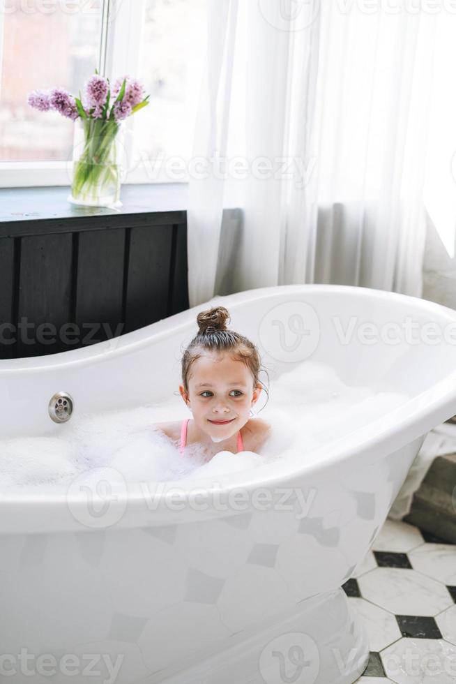 menina feliz se divertindo no banho com espuma em casa foto