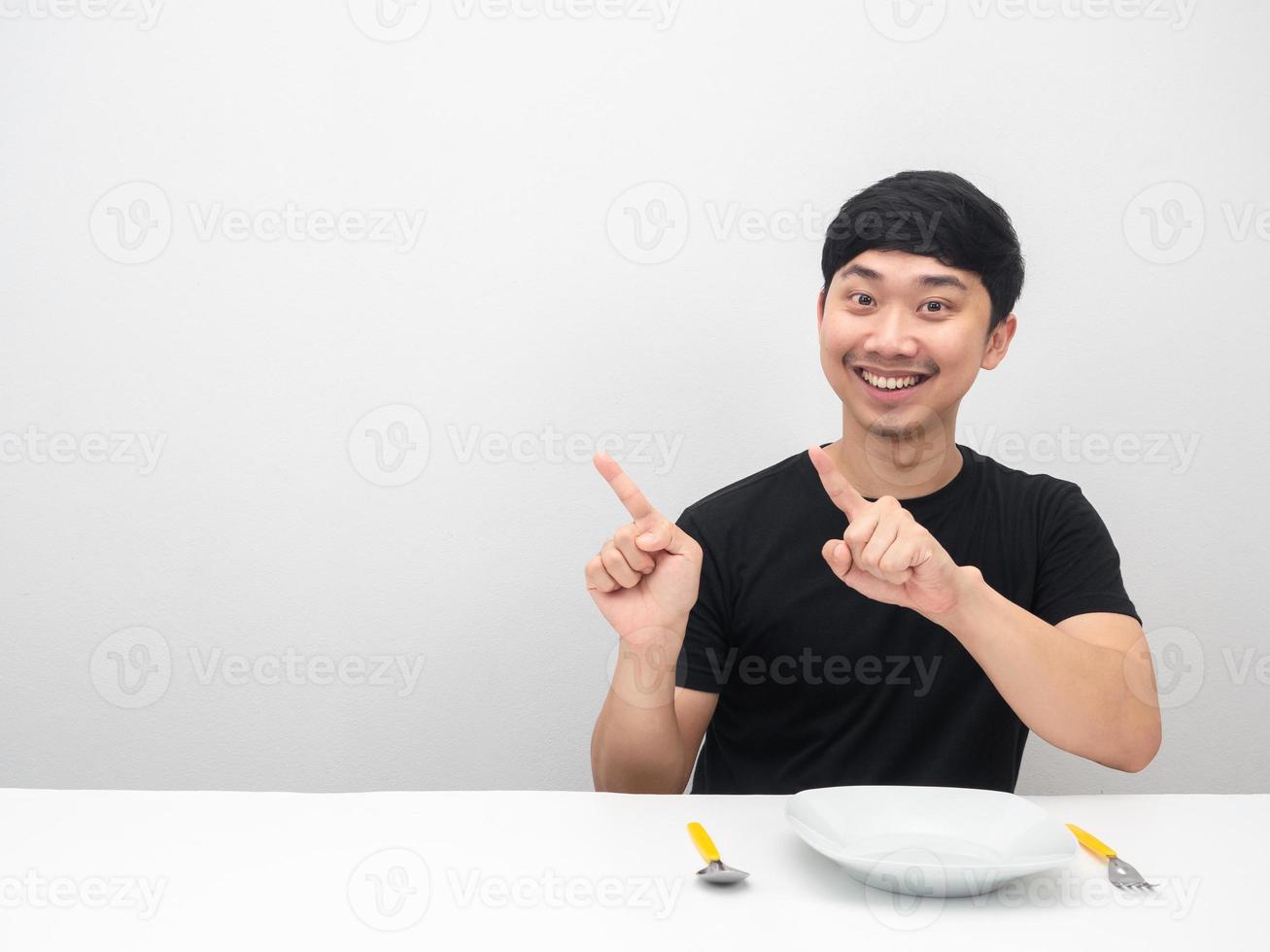 homem asiático sorrindo, sente-se à mesa com o dedo apontador de talheres no espaço da cópia foto