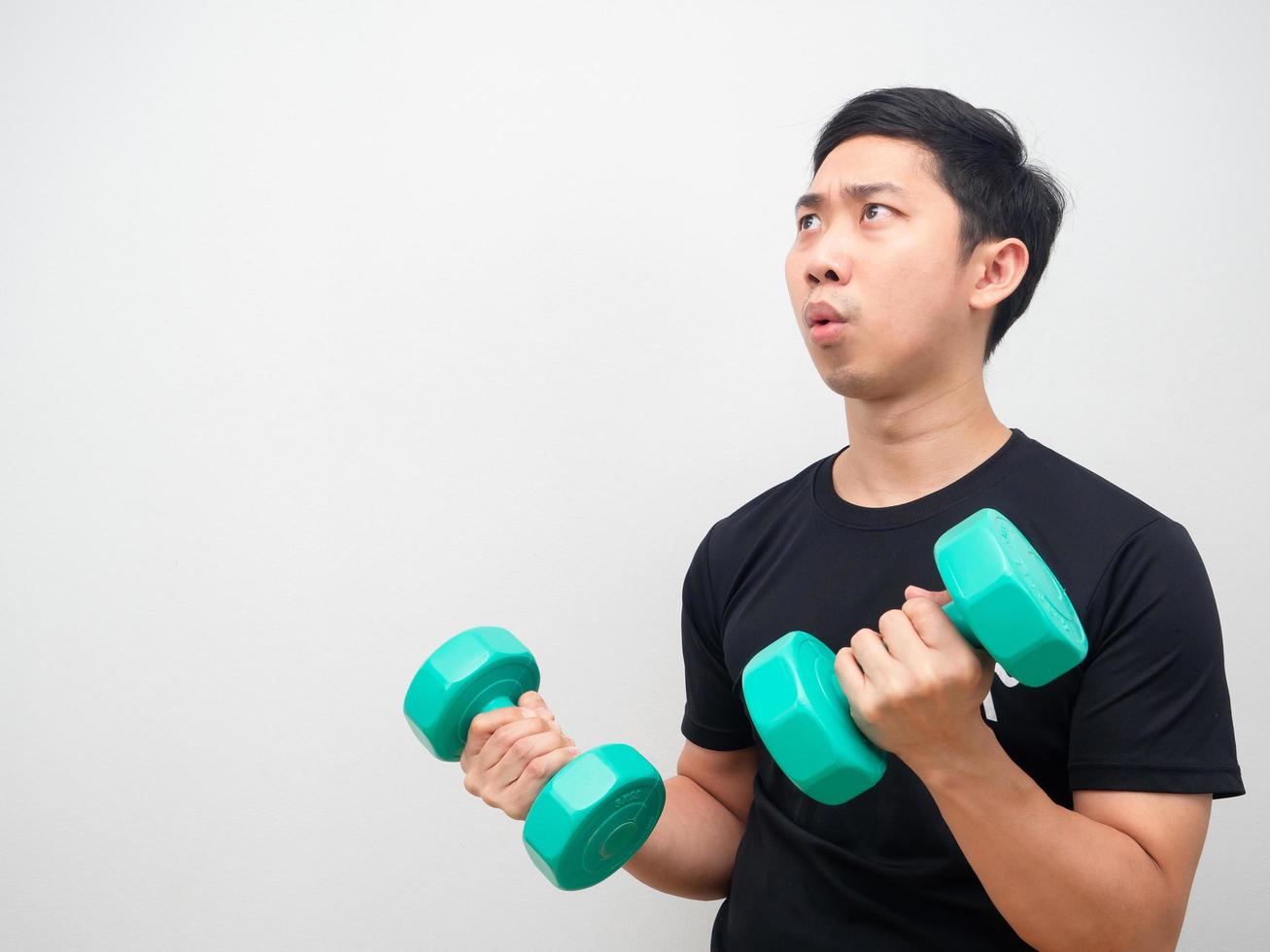 homem asiático segurando drumbbell sentindo-se maravilhado e olhando para o fundo branco do espaço da cópia foto