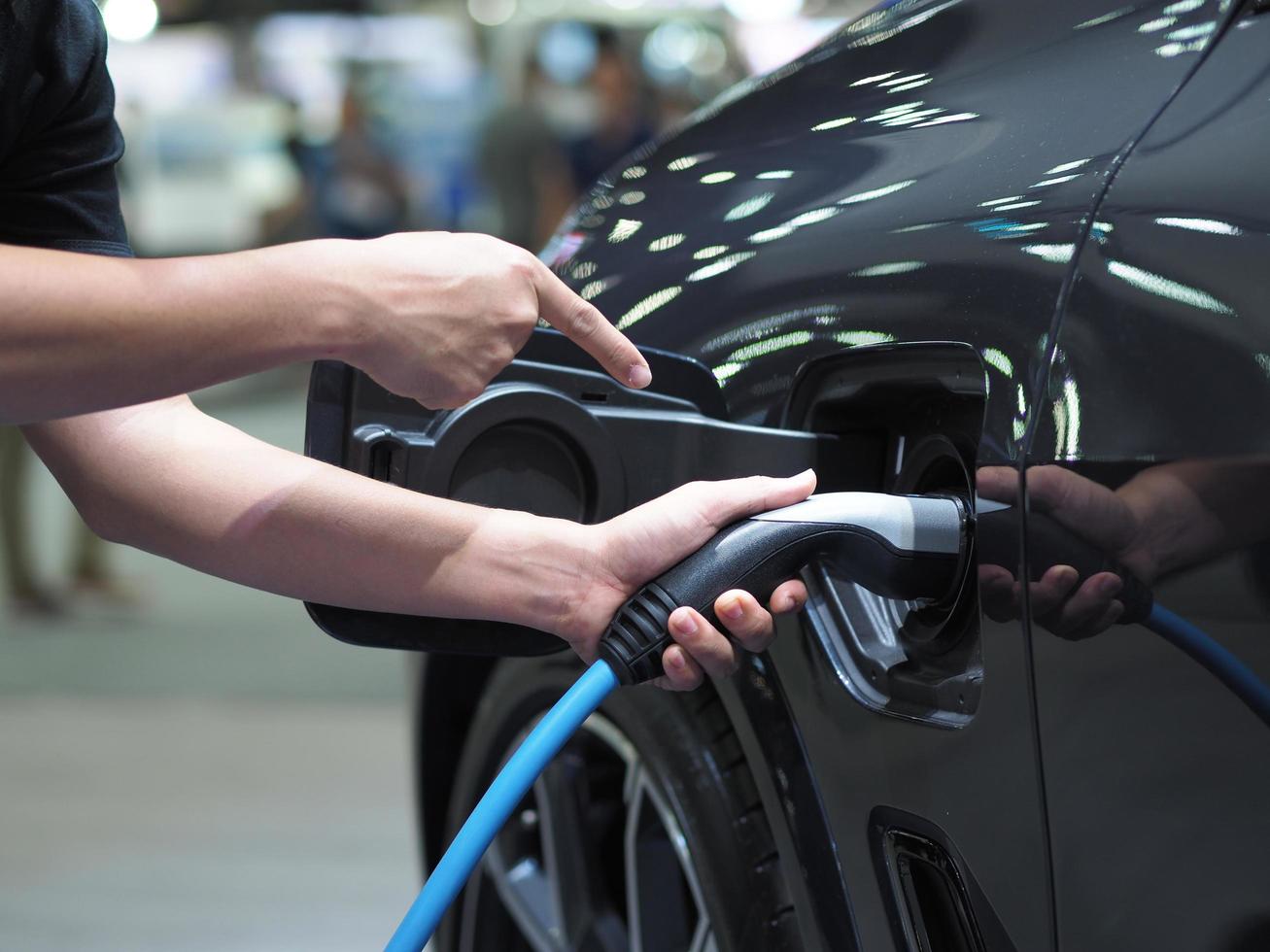 segure a mão e aponte o dedo para o plugue do veículo de carregamento elétrico e o sinalizador de luz para recarregar a bateria do carro de cor preta energia limpa para o conceito futuro foto