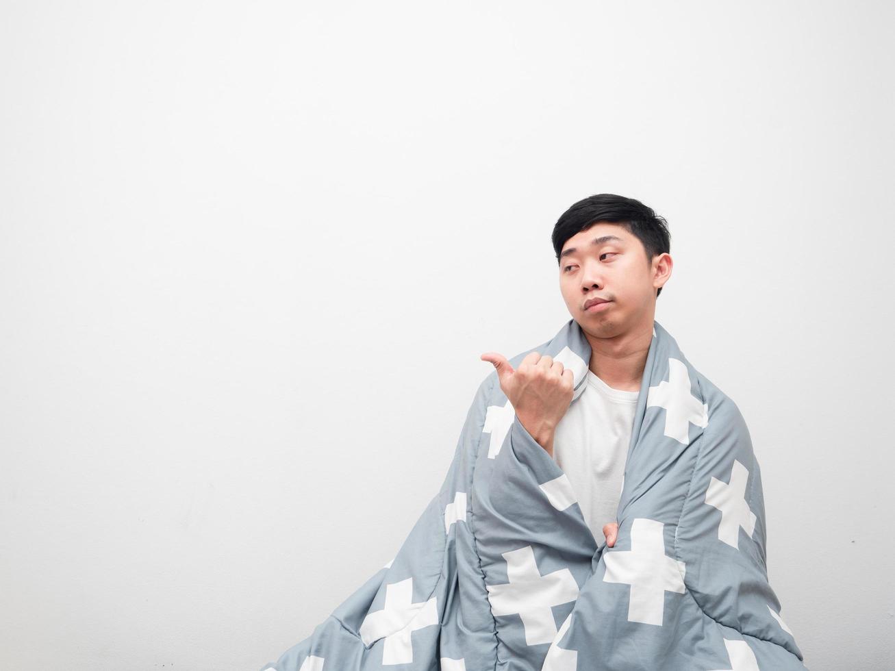 homem asiático cobre corpo por cobertor e rosto entediado aponta dedo espaço para cópia do lado esquerdo no fundo branco, não quer acordar o conceito foto