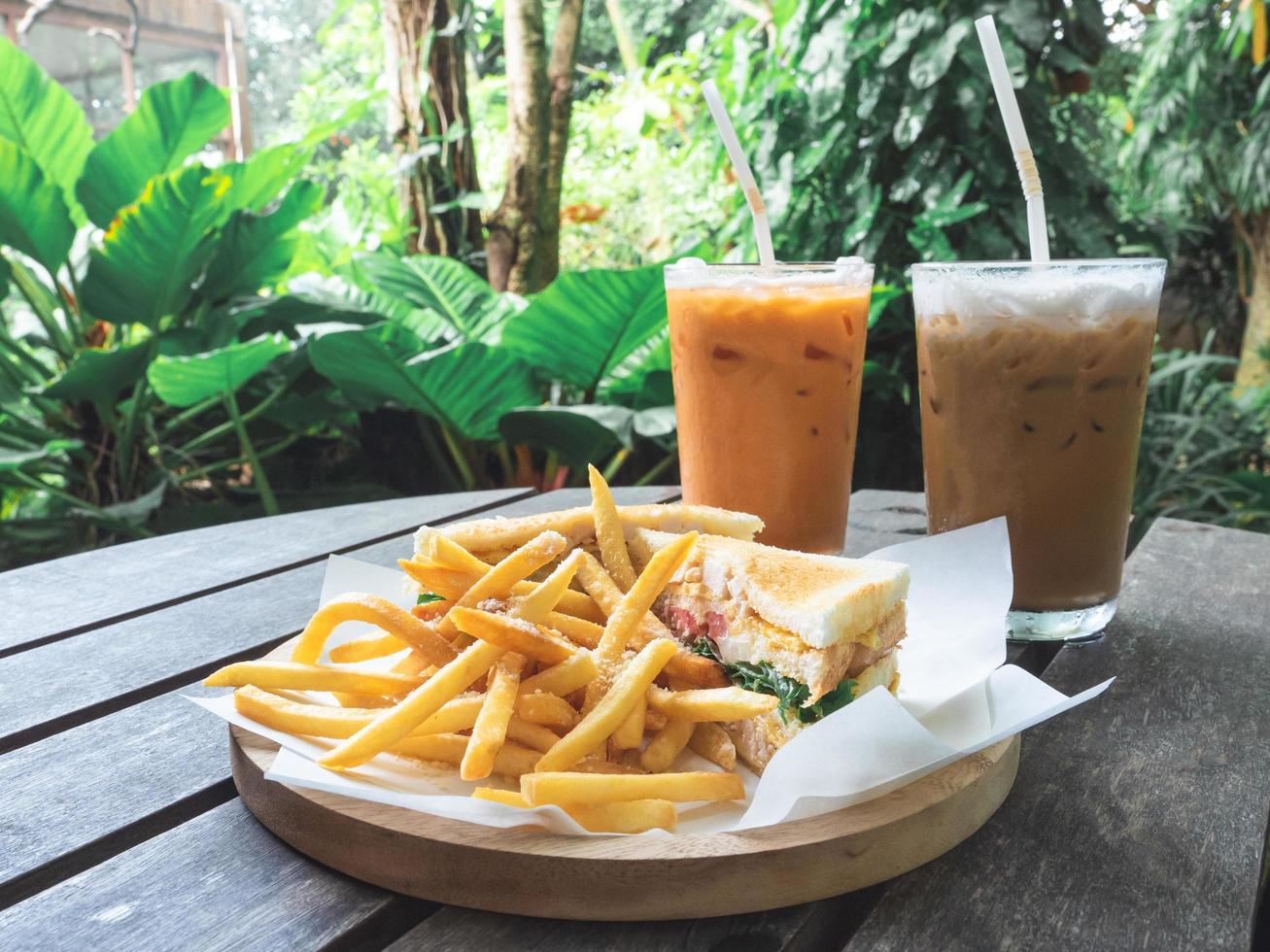 francês frito com sanduíche em placa de madeira café da manhã com chá tailandês e leite de café branco na mesa de madeira no café e fundo de planta verde foto