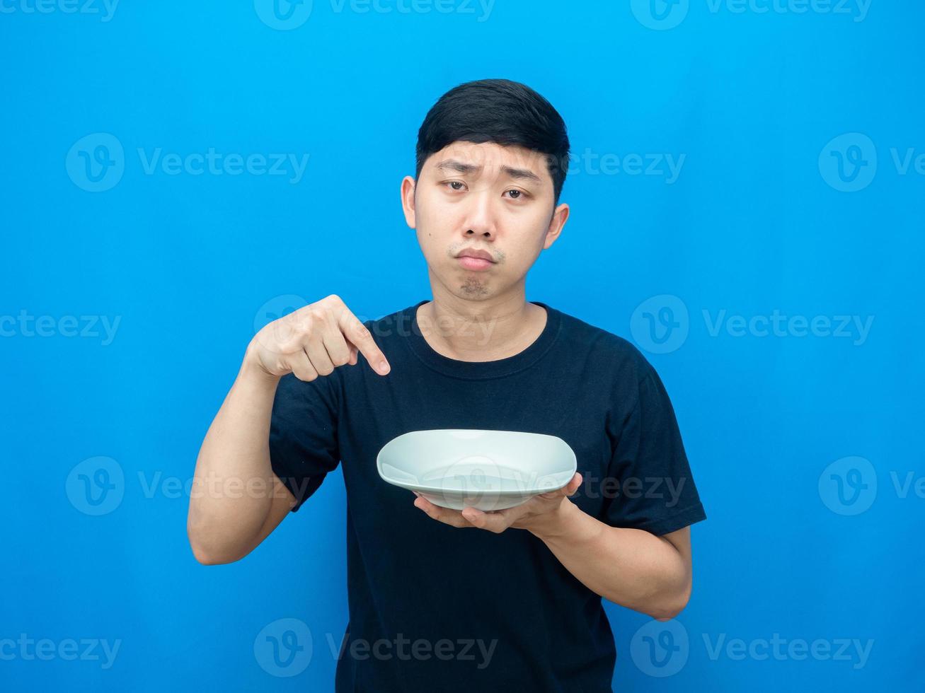 homem com fome aponta o dedo para o prato na mão cara triste fundo azul foto