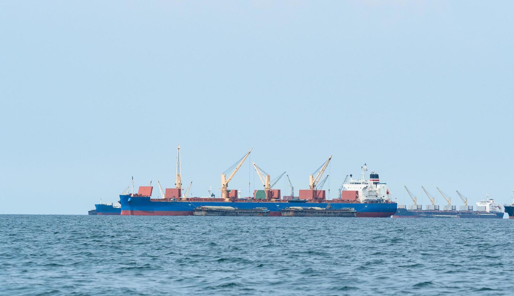 grande navio de carga cor vermelha com grande guindaste no oceano azul e paisagem de céu azul, barco industrial no conceito logístico do mar foto