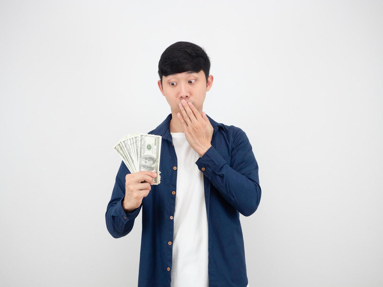 homem asiático olhando para um monte de dinheiro na mão e fechando a boca com a mão se sente maravilhado no fundo branco isolado foto