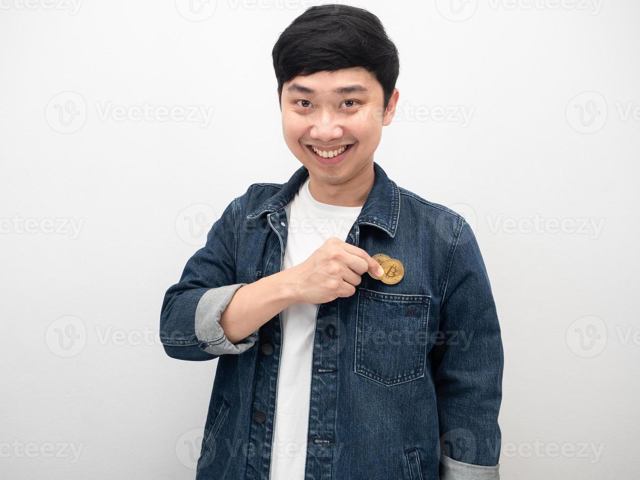 homem asiático de retrato sorri e guarda bitcoin no bolso da calça jeans foto