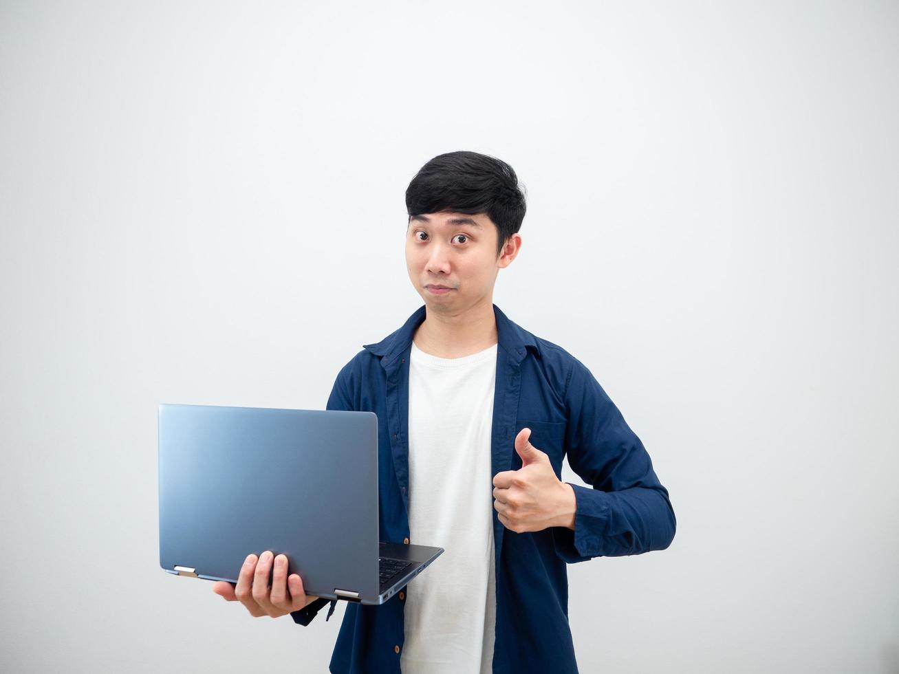 homem bonito asiático segurando laptop mostra o polegar para cima rosto confiante no fundo da parede branca foto
