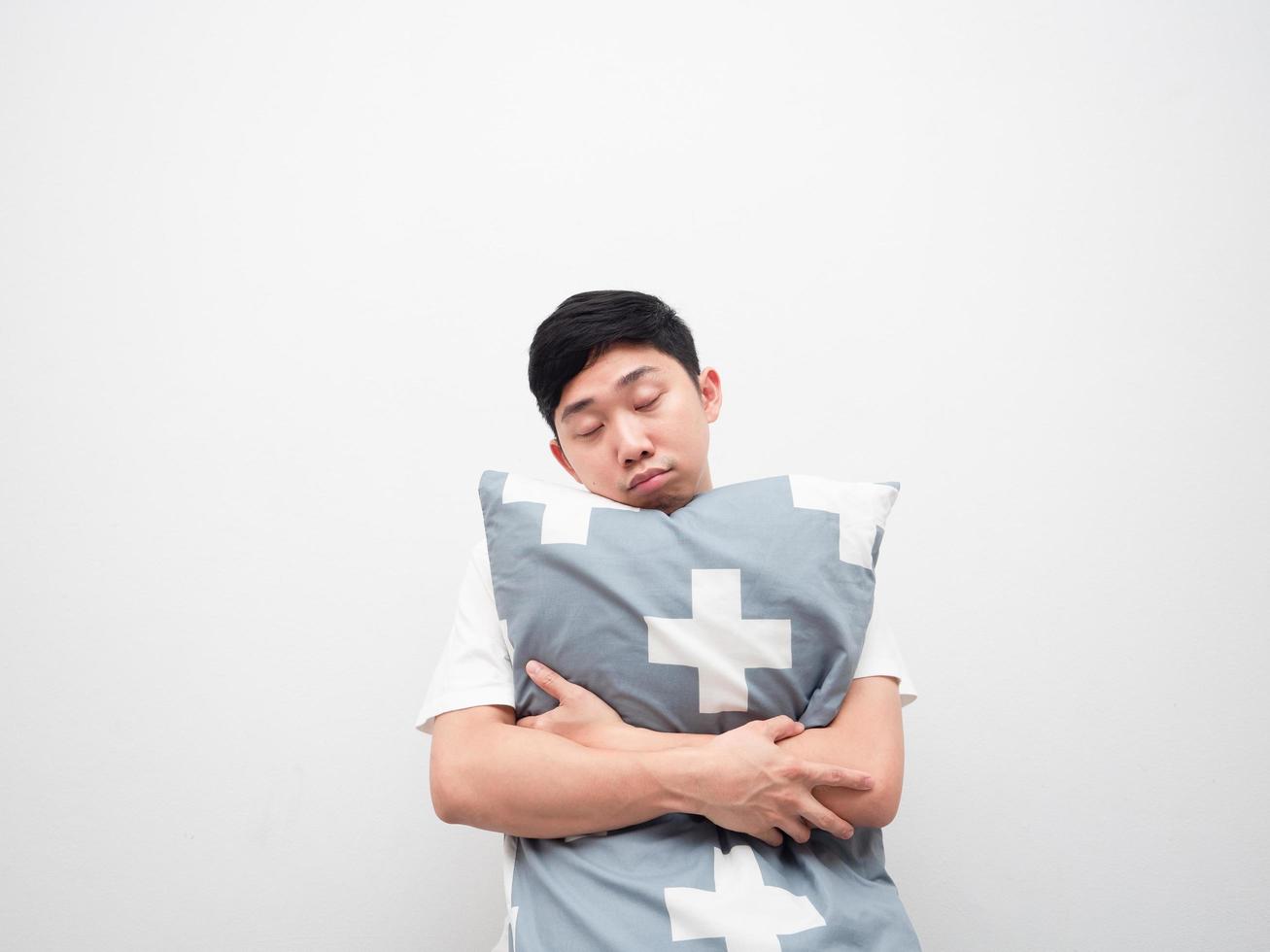 travesseiro de abraço de rosto sonolento de homem asiático no conceito preguiçoso de fundo branco foto