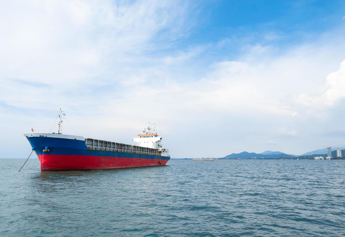 navio cargueiro cor azul vermelha no fundo da montanha oceano e ilha com céu azul e paisagem nublada foto